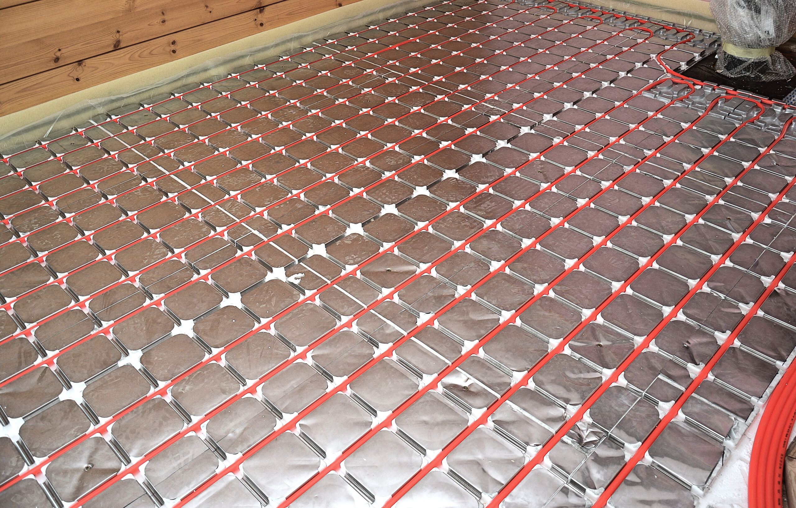 Underfloor radiant heating mats with red tubing laid over a metal grid, ready for flooring.