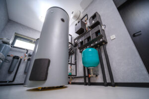 Industrial mechanical room with a tall gray cylindrical tank, teal expansion tank, and exposed piping.